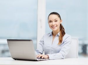 Smiling, professionally-attired young woman sits before laptop computer